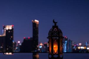 linterna que tiene el símbolo de la luna en la parte superior con el fondo de la ciudad nocturna para la fiesta musulmana del mes sagrado del ramadán kareem. foto