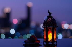 Selective focus of lantern that have moon symbol on top and small plate of dates fruit with city bokeh light background for the Muslim feast of the holy month of Ramadan Kareem. photo