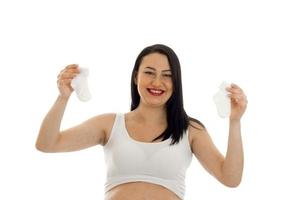 cheerful young pregnant brunette woman with two little socks in hands smiling isolated on white background photo