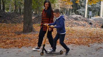 mère aide son fils à monter sur un scooter lors de la chaude journée d'automne dans le parc video