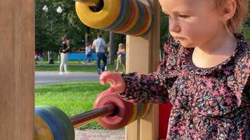 encantadora menininha loira brinca com círculos multicoloridos em um parquinho video