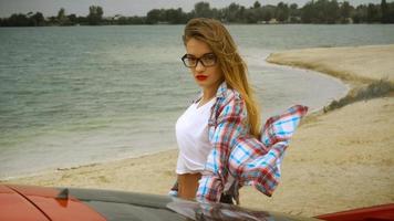 hermosa rubia con gafas se para en el auto rojo foto