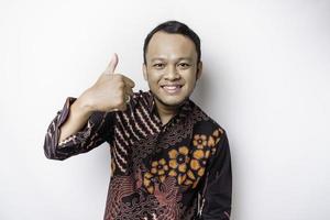 Excited Asian man wears batik shirt, gives thumbs up hand gesture of approval, isolated by white background photo