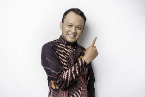 Excited Asian man wearing batik shirt pointing at the copy space on top of him, isolated by white background photo