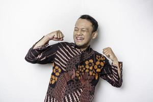 A young Asian man with a happy successful expression wearing batik shirt isolated by white background photo