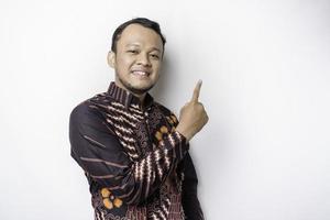 Excited Asian man wearing batik shirt pointing at the copy space on top of him, isolated by white background photo