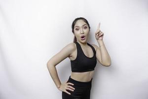 Shocked Asian sporty woman wearing sportswear pointing at the copy space on top of her, isolated by white background photo