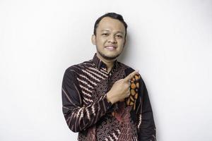 Excited Asian man wearing batik shirt pointing at the copy space beside him, isolated by white background photo