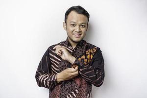 A stylish Asian man wearing batik shirt buttoning up shirt sleeves while standing against white background photo