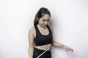 Portrait of cheerful young Asian woman in sportswear measuring waist with tape, feeling happy about losing weight at home. Healthy lifestyle, sports and slimming diet concept photo