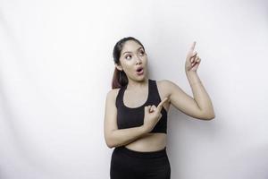 Shocked Asian sporty woman wearing sportswear pointing at the copy space on top of her, isolated by white background photo