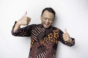 Excited Asian man wears batik shirt, gives thumbs up hand gesture of approval, isolated by white background photo