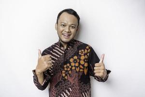 Excited Asian man wears batik shirt, gives thumbs up hand gesture of approval, isolated by white background photo