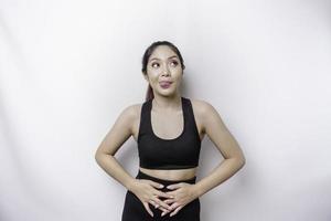 A sporty Asian woman is hungry and touching her belly while looking aside thinking what to eat photo
