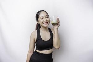 Joyful sporty Asian woman wearing sportswear with glass of tasty green smoothie, isolated on white background. photo