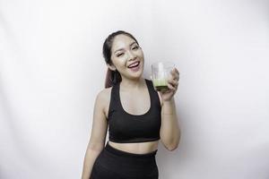 alegre mujer asiática deportiva que usa ropa deportiva con un vaso de sabroso batido verde, aislada de fondo blanco. foto