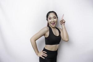 Excited Asian sporty woman wearing sportswear pointing at the copy space on top of her, isolated by white background photo