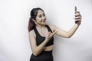 A portrait of a sporty Asian woman wearing a sportswear and holding her phone, isolated by white background photo