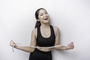 retrato de una alegre joven asiática con ropa deportiva que mide la cintura con cinta, sintiéndose feliz por perder peso en casa. estilo de vida saludable, deportes y concepto de dieta adelgazante foto