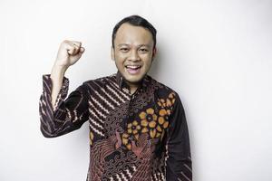 A young Asian man with a happy successful expression wearing batik shirt isolated by white background photo