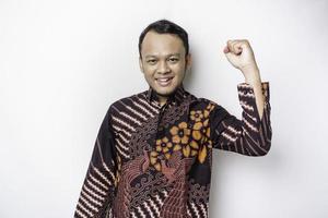 A young Asian man with a happy successful expression wearing batik shirt isolated by white background photo