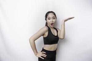 mujer deportiva asiática sorprendida usando ropa deportiva apuntando al espacio de copia encima de ella, aislada por fondo blanco foto