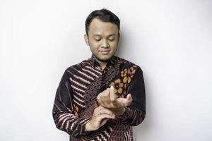 A stylish Asian man wearing batik shirt buttoning up shirt sleeves while standing against white background photo