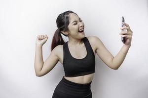 A young sporty Asian woman with a happy successful expression wearing sportswear and holding smartphone isolated by white background photo