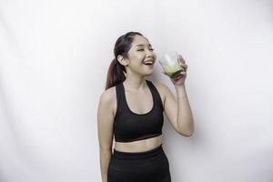 Joyful sporty Asian woman wearing sportswear with glass of tasty green smoothie, isolated on white background. photo