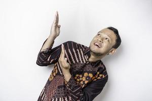 Excited Asian man wearing batik shirt pointing at the copy space on top of him, isolated by white background photo