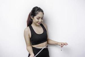 Portrait of cheerful young Asian woman in sportswear measuring waist with tape, feeling happy about losing weight at home. Healthy lifestyle, sports and slimming diet concept photo