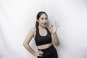 una mujer asiática deportiva emocionada que usa ropa deportiva está dando un gesto de mano bien aislado por un fondo blanco foto