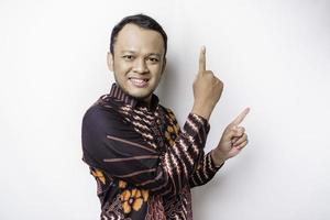 Excited Asian man wearing batik shirt pointing at the copy space on top of him, isolated by white background photo