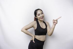 Excited Asian sporty woman wearing sportwear pointing at the copy space beside her, isolated by white background photo