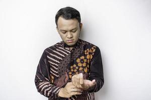 A stylish Asian man wearing batik shirt buttoning up shirt sleeves while standing against white background photo