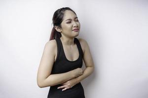 una joven enferma enferma que usa ropa deportiva sostiene la mano en el estómago sufre dolor aislado de fondo blanco foto