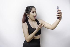 una mujer asiática deportiva insatisfecha se ve descontenta usando ropa deportiva expresiones faciales irritadas sosteniendo su teléfono foto