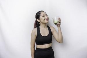 alegre mujer asiática deportiva que usa ropa deportiva con un vaso de sabroso batido verde, aislada de fondo blanco. foto