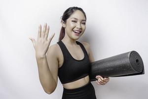 Young Asian beautiful sporty woman carrying yoga mat, isolated white background inviting to join with hand. Happy that you came photo