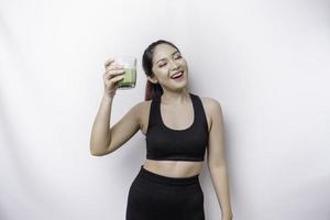Joyful sporty Asian woman wearing sportswear with glass of tasty green smoothie, isolated on white background. photo