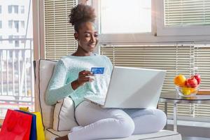 Picture showing pretty woman shopping online with credit card. African American woman holding credit card and using laptop. Online shopping concept photo