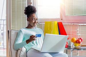 Young woman holding credit card and using laptop computer. Online shopping concept. Happy black woman doing online shopping at home photo