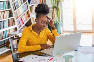 Young frustrated woman working at office desk in front of laptop suffering from chronic daily headaches, treatment online, appointing to a medical consultation, electromagnetic radiation, sick pay photo