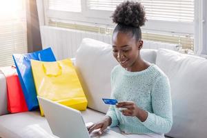 Woman is holding credit card and using laptop computer. Online shopping concept. Young African American girl is buying fashion items by using credit card photo