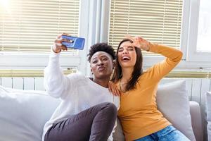 Two beautiful young women take selfie on sunny day at home. Girlfriends. Communication and gossip. Lovable caucasian and African American girls expressing positive emotions to camera. photo