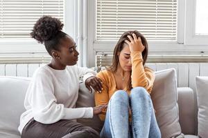 chica triste y amigos de apoyo tratando de resolver un problema. dos tristes mujeres diversas hablando en casa. amigas apoyándose mutuamente. problemas, amistad y concepto de cuidado foto