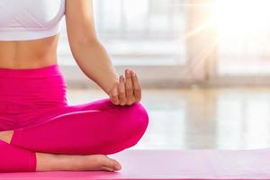 Young attractive smiling woman practicing yoga, sitting in Half Lotus exercise, Ardha Padmasana pose, working out, wearing sportswear, meditation session, indoor full length, home interior photo