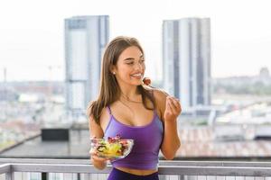 joven caucásica comiendo ensalada al aire libre al atardecer. dieta saludable. hermosa mujer sonriente comiendo ensalada vegetariana orgánica fresca. concepto de alimentación saludable, alimentación y estilo de vida. Salud y Belleza foto