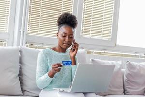 Woman is holding credit card and using laptop computer calling support. Online shopping concept. Young African American girl is buying fashion items by using credit card photo