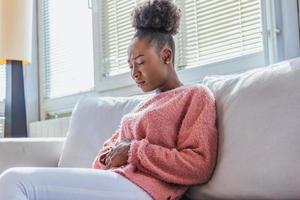 Woman in painful expression holding hands against belly suffering menstrual period pain, lying sad on home bed, having tummy cramp in female health concept photo